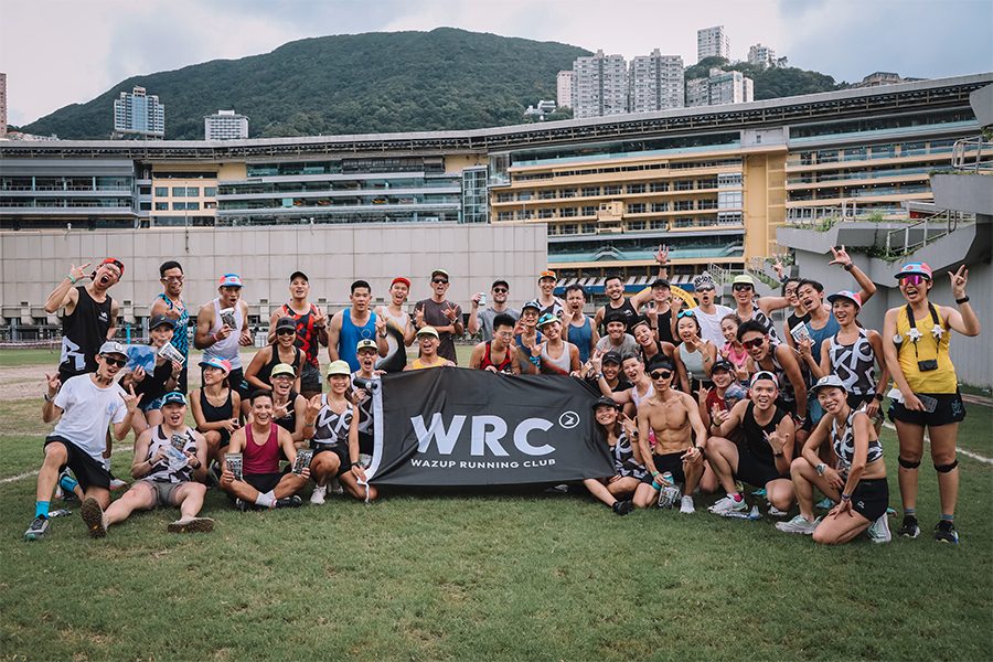 A group of people from Wazup Running Club posing for a group photo on the grass during the day