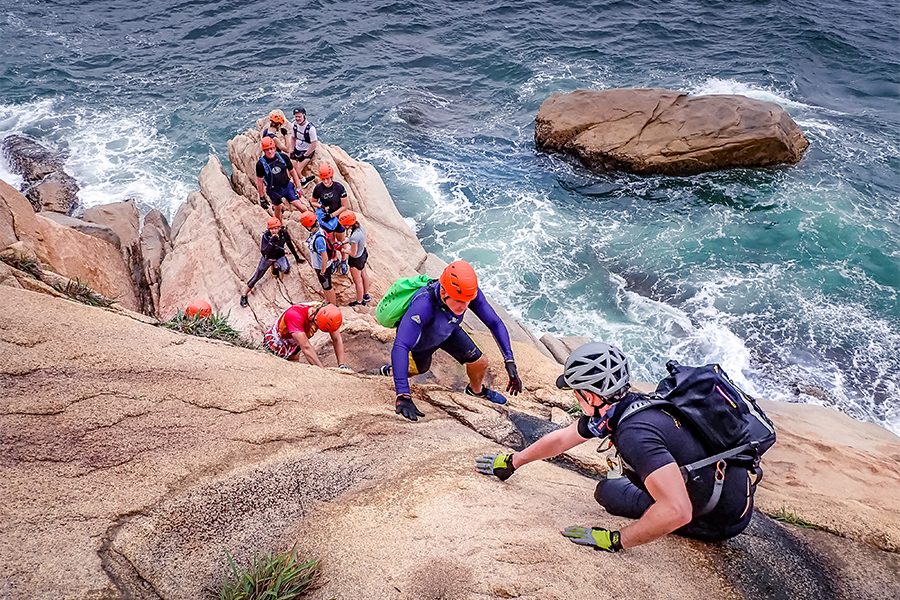 A group of people coasteering, climbing rocks by the open sea