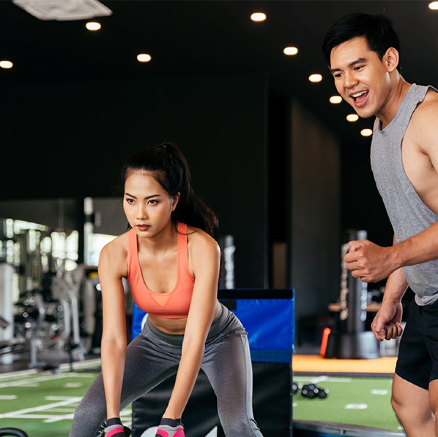 A woman performing functional training in a gym while a fitness trainer encourages her during a workout session