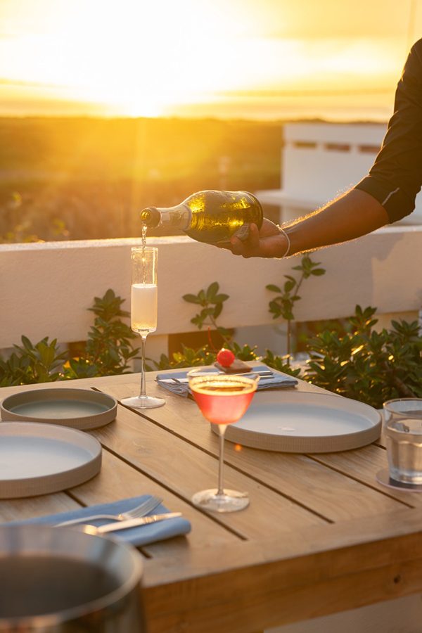 A server pouring a tall glass of beverage at the table with a view of the sunset on Charlie's rooftop bar in Sri Lanka