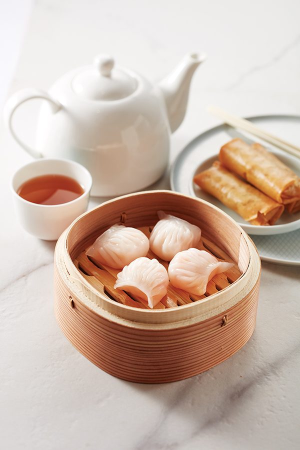 Dim sum in a bamboo steamer next to a pot of tea
