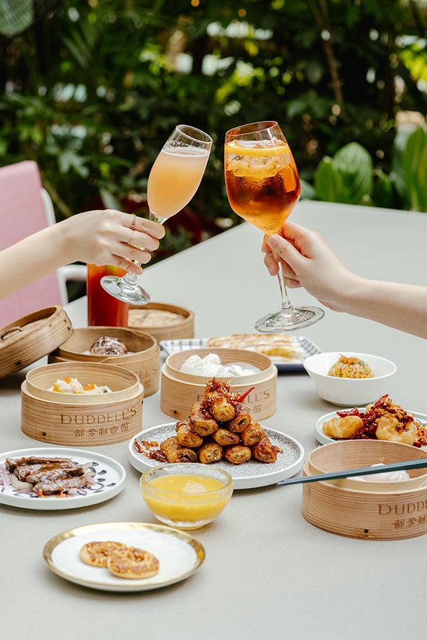 People clink glasses over an outdoor table laden with dim sum 