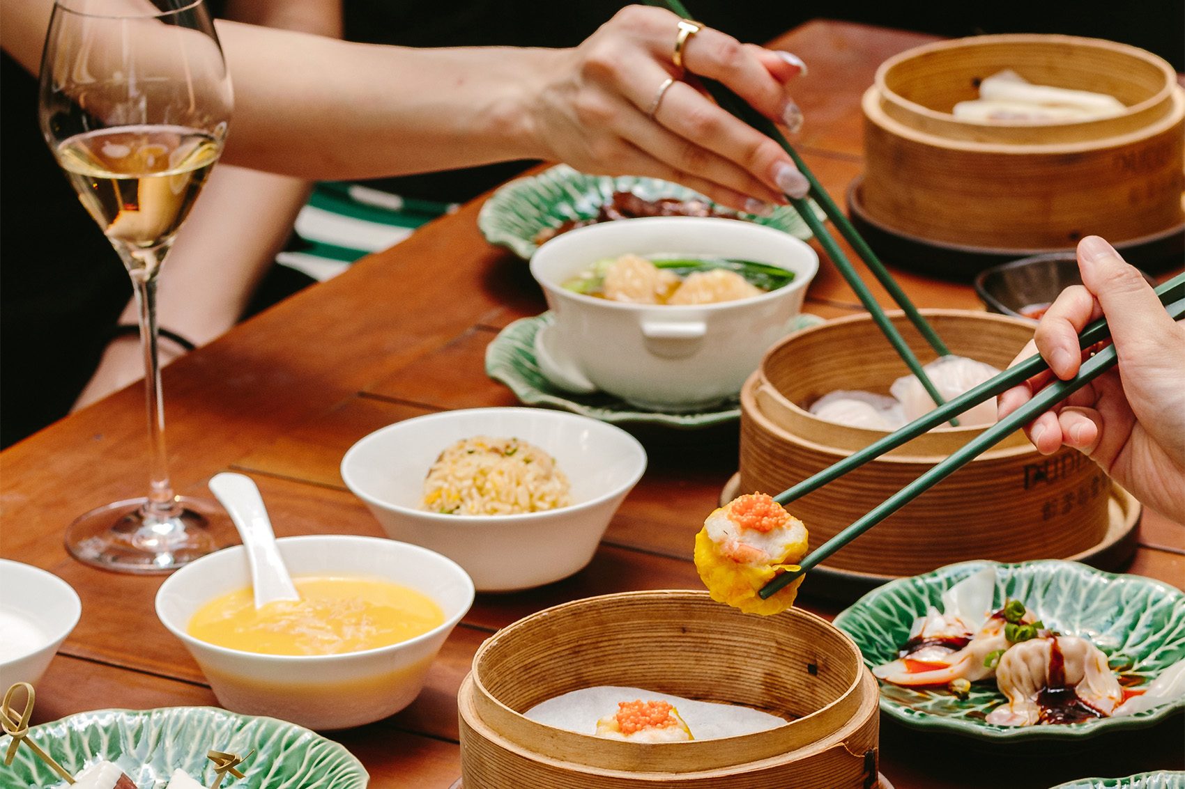 People using chopsticks to take dim sum from baskets on a table 