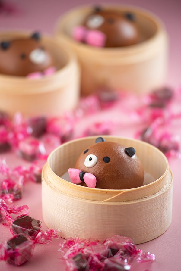 A bamboo steamer containing a steamed bun decorated to resemble a teddy bear 