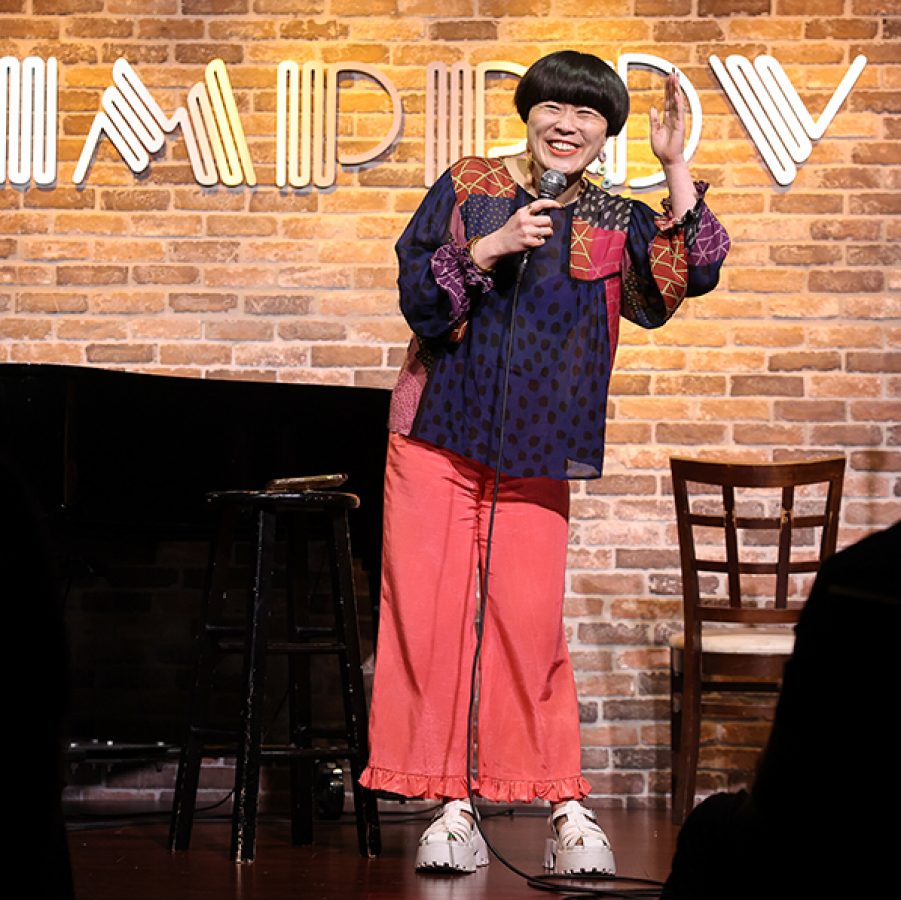 A person is doing stand-up comedy at the Friendly House Annual Comedy Funstival Friendstival.