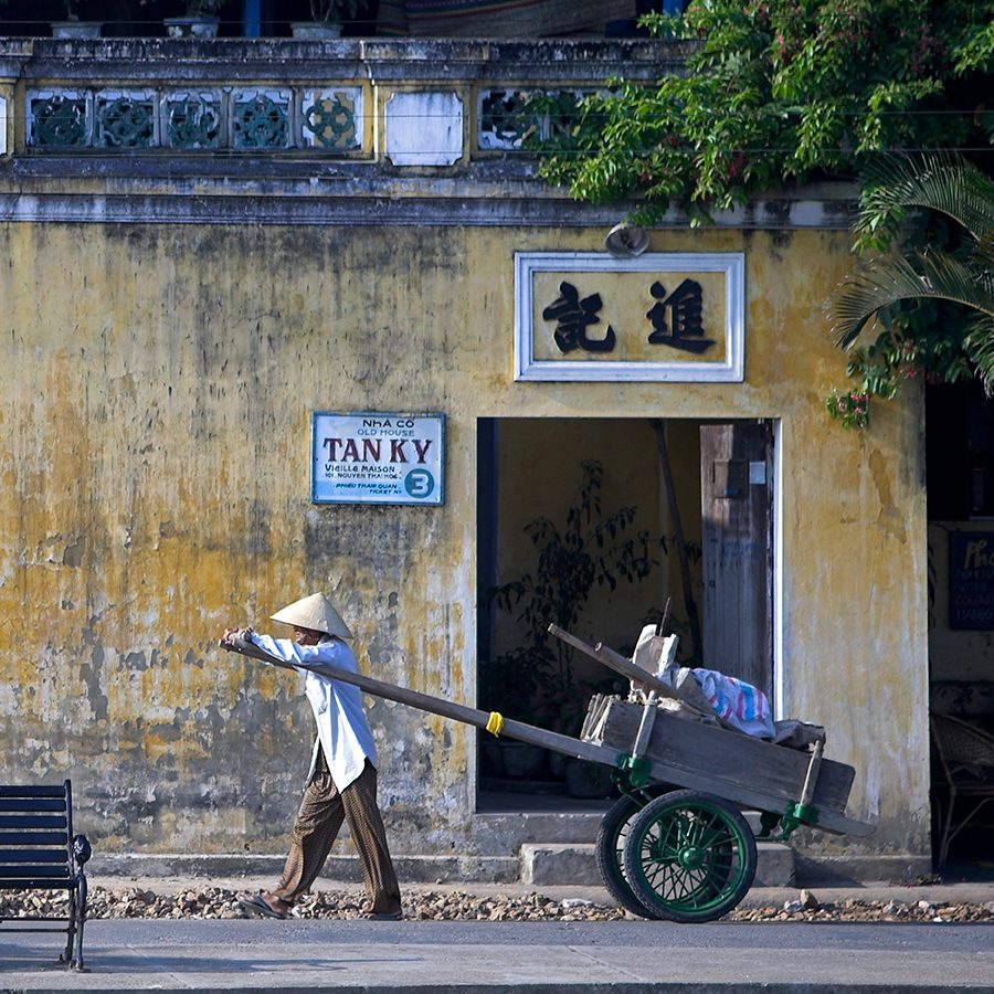 A man in conical hat pulls hand cart
