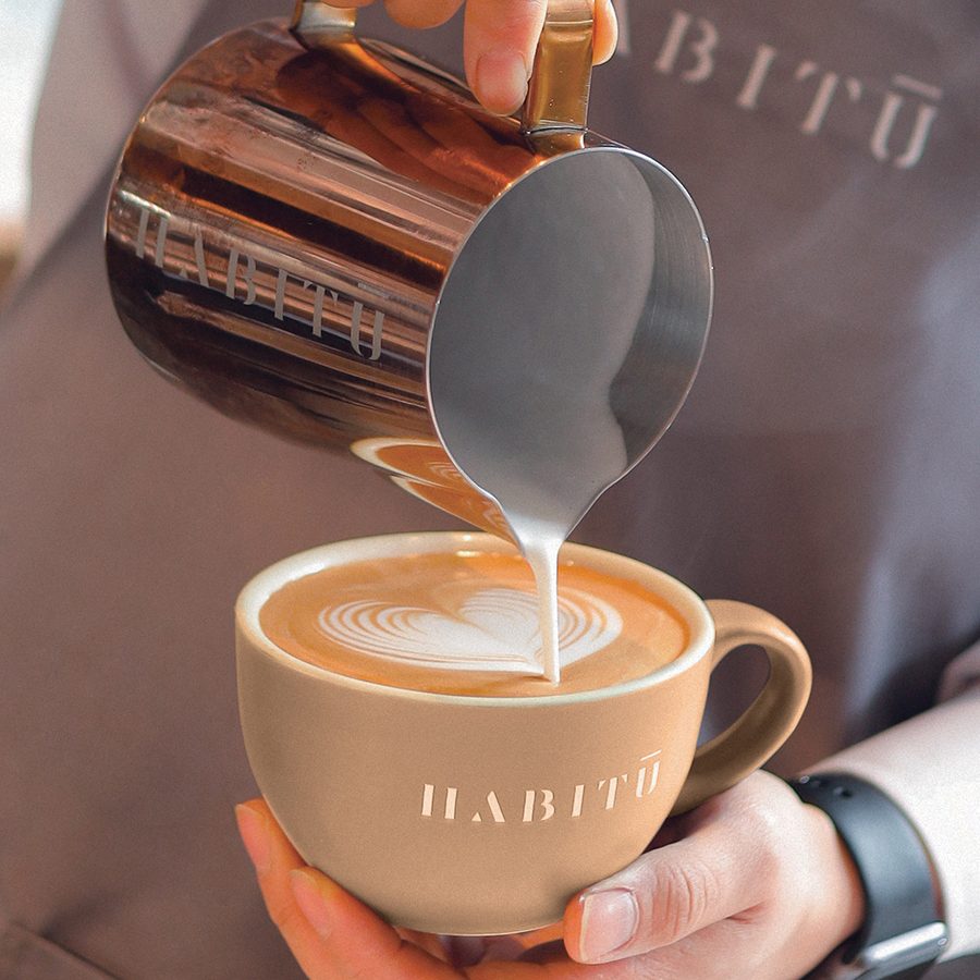 A barista making latte art at Habitū table  