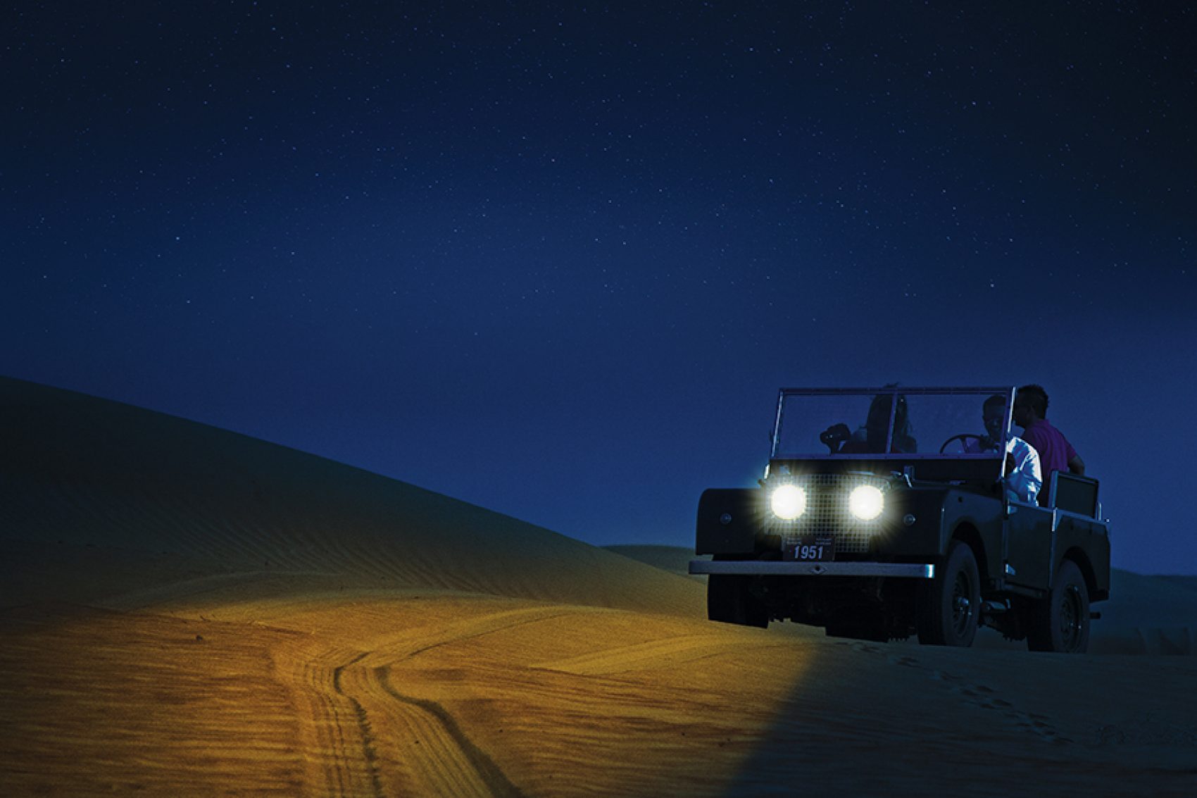 A man driving a jeep in the dessert on a sand dune in Dubai, UAE