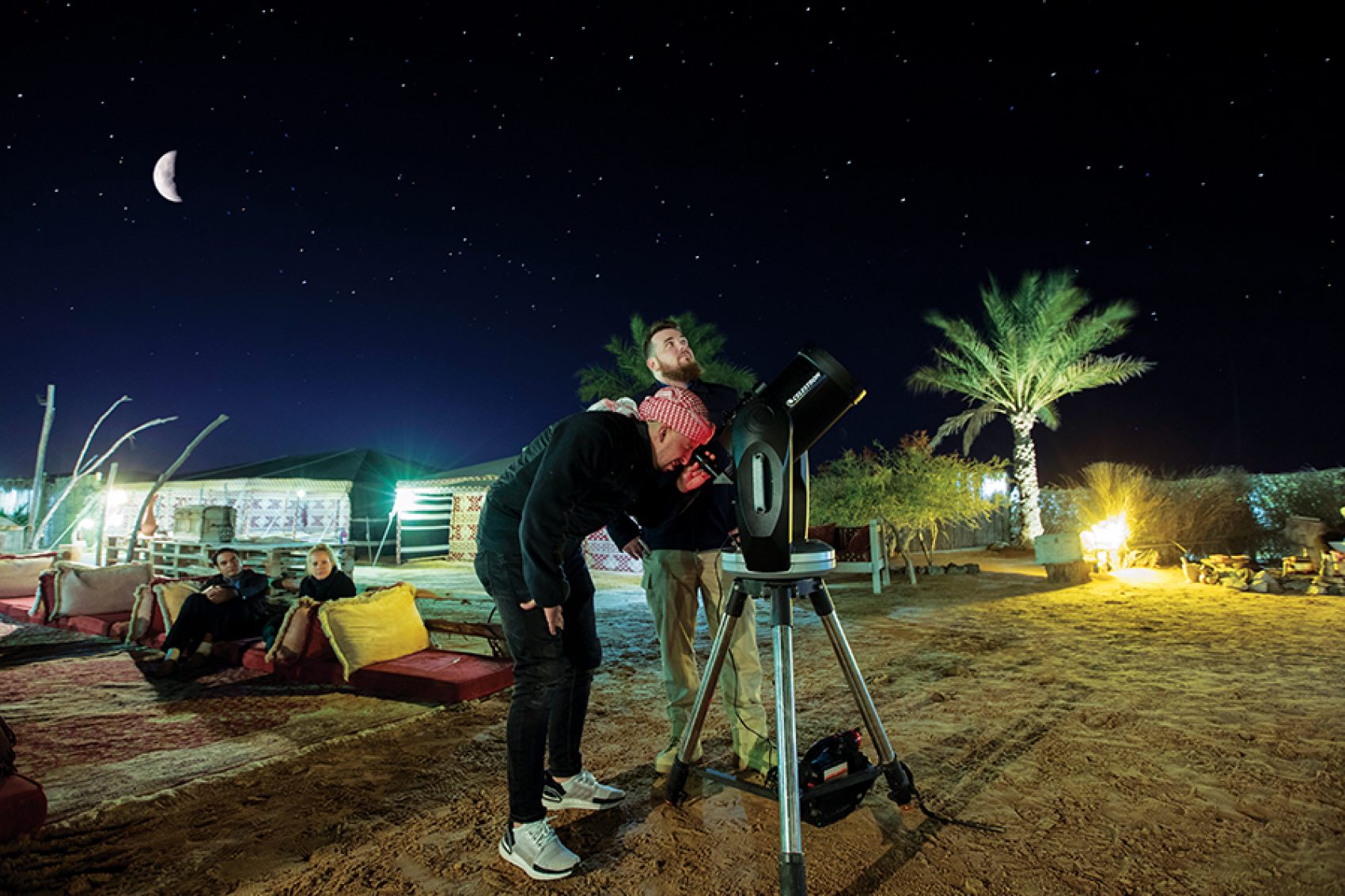 Two men looking up at the night sky, stargazing through a telescope in the desert in Dubai, UAE