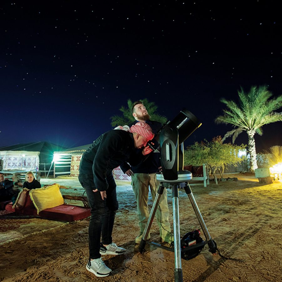 Two men looking up at the night sky, stargazing through a telescope in the desert in Dubai, UAE