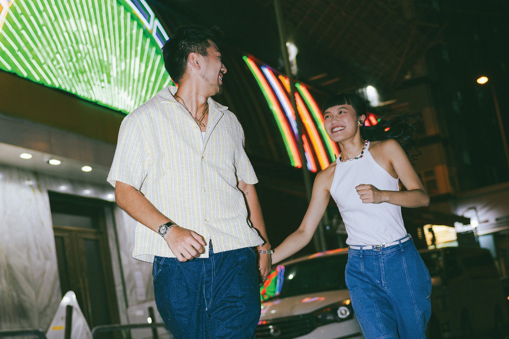 A couple of man and woman smiling and running in the street at night in Hong Kong
