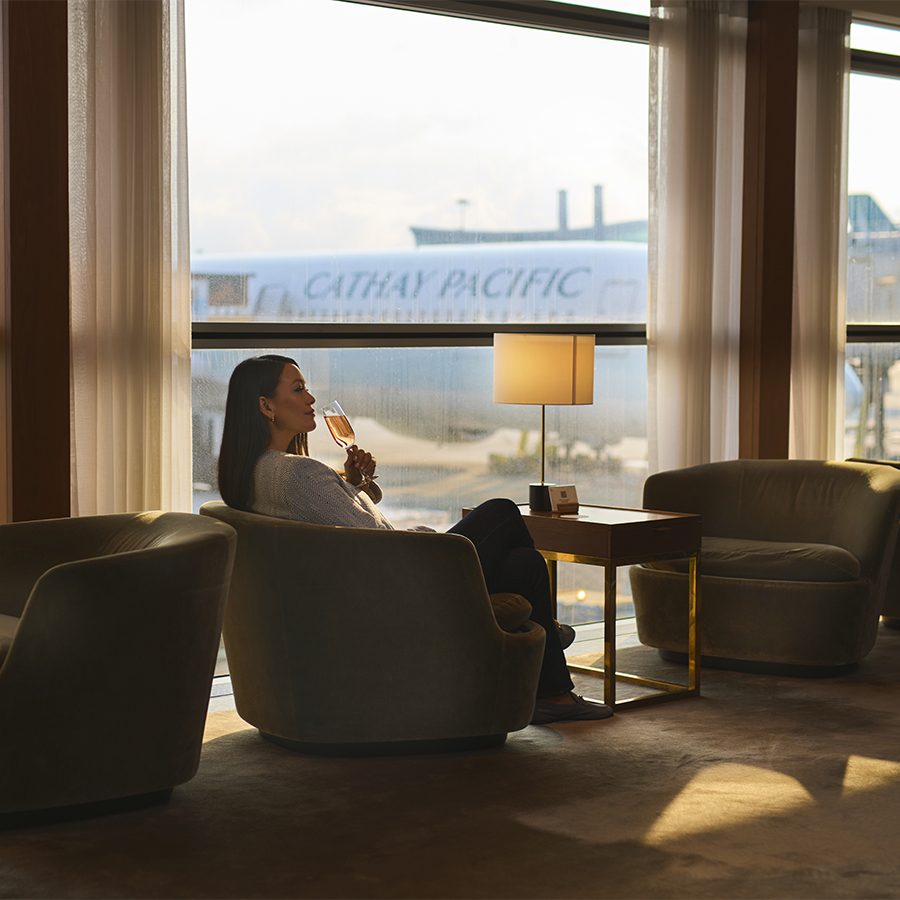 A woman sitting and drinking from a wine glass at a Cathay Pacific airport lounge in Hong Kong 