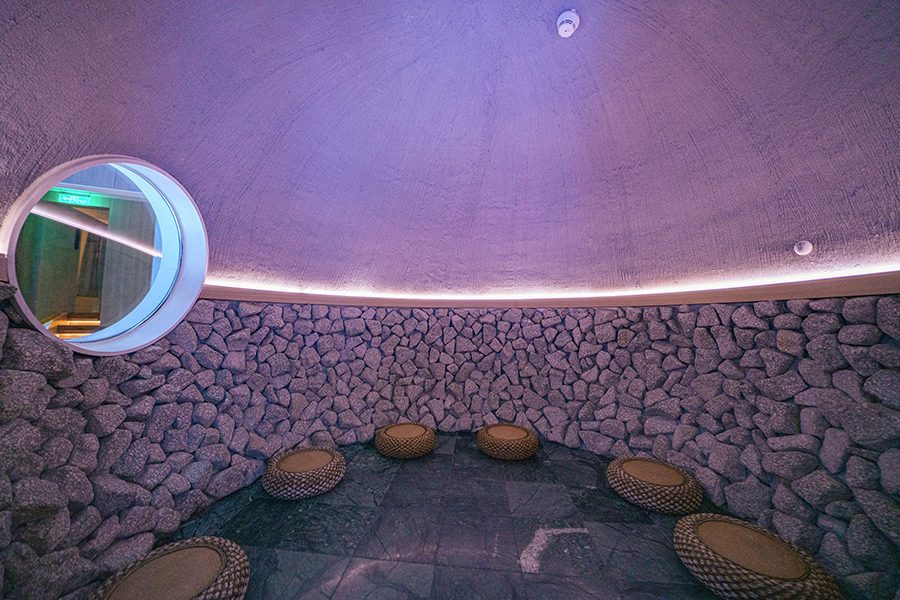 The inside of a volcanic stone steam room in Heat Joy Spa with round floor cushions and a circular window