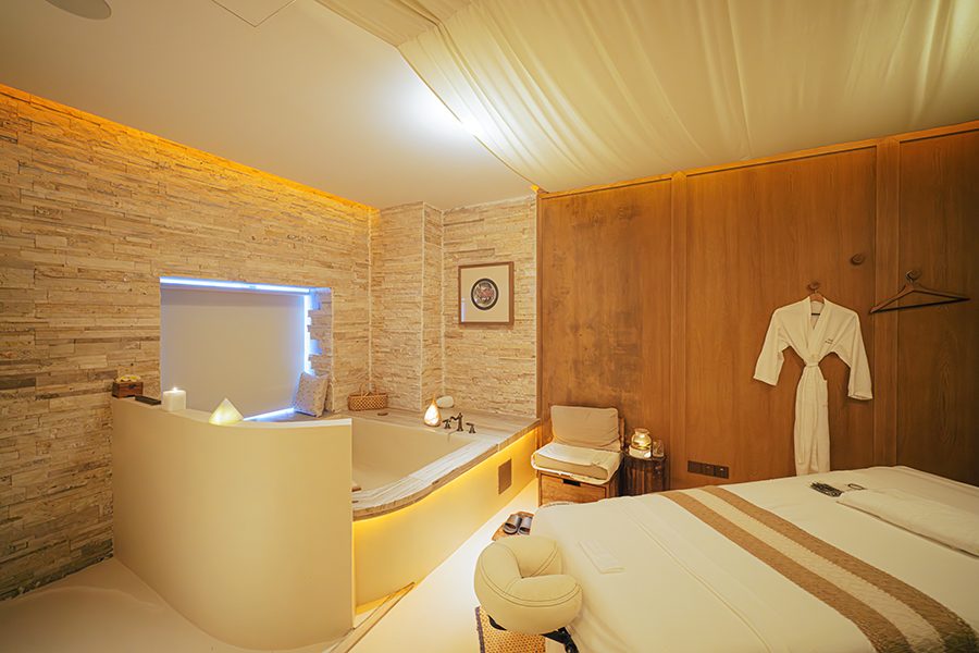 A room in Hui Spa with wood walls, a bed, a bathtub, candles, and a bathrobe on a hanger