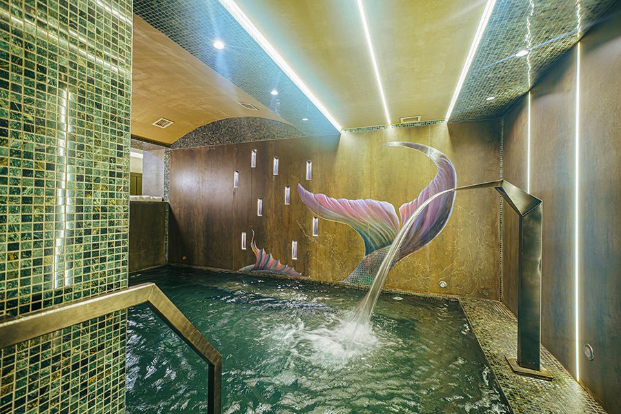 An indoor pool in Mi Spa with a water fountain on the right and a colourful tail design on the wall