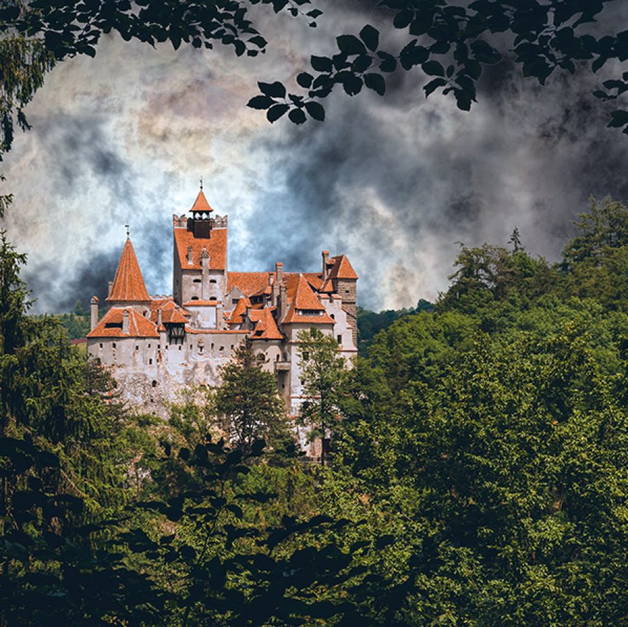 Bran Castle, Transylvania, peeping through green trees under a dramatic cloudy sky.
