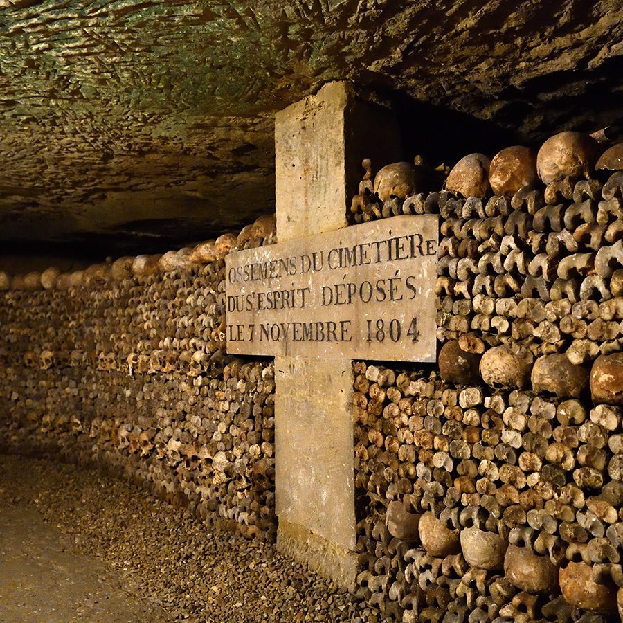 A wall of skulls surrounding a cross-shaped sign in the Paris Catacombs. 