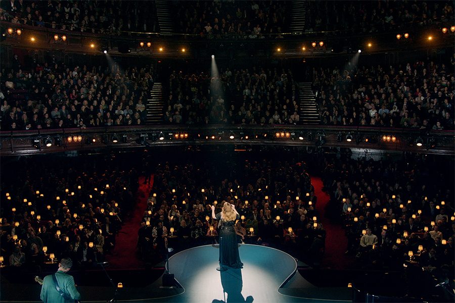 A female singer performs to a rapt audience onstage at The London Palladium. She is accompanied by two musicians standing at stage left