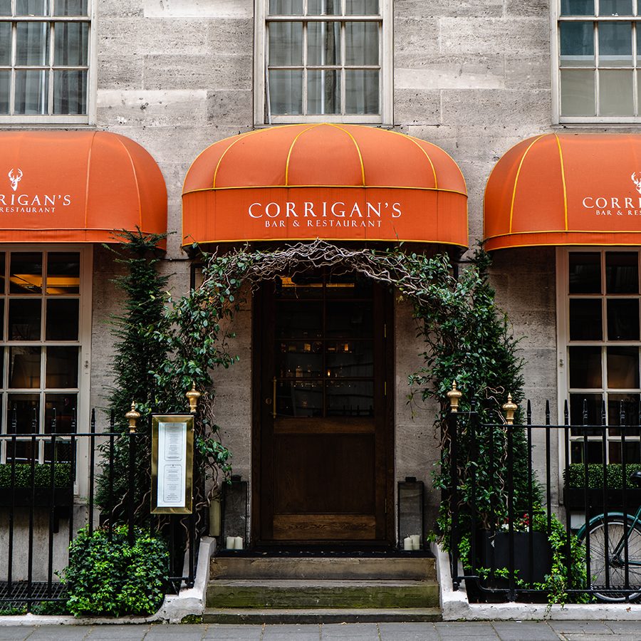 The entrance of Corrigan’s Mayfair in London: a dark wooden door under orange awning