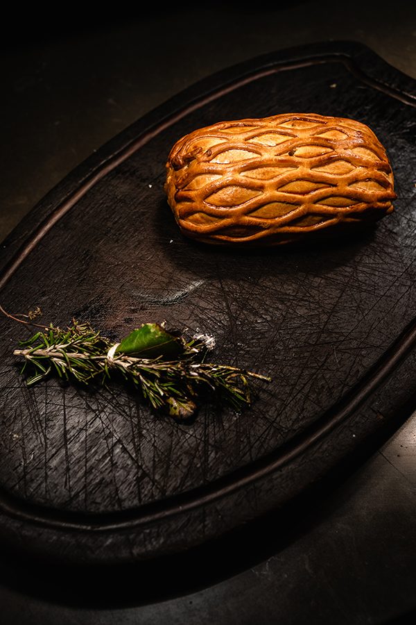  A beef Wellington served with a sprig of herbs on a dark wooden board at Corrigan’s Mayfair in London