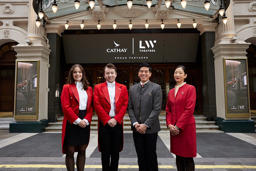Two Red Coat Concierge staff and two members of Cathay’s cabin crew stand in a row in front of the London Palladium. The Cathay and Lloyd Webber Theatres logos appear in white on a black banner in the background