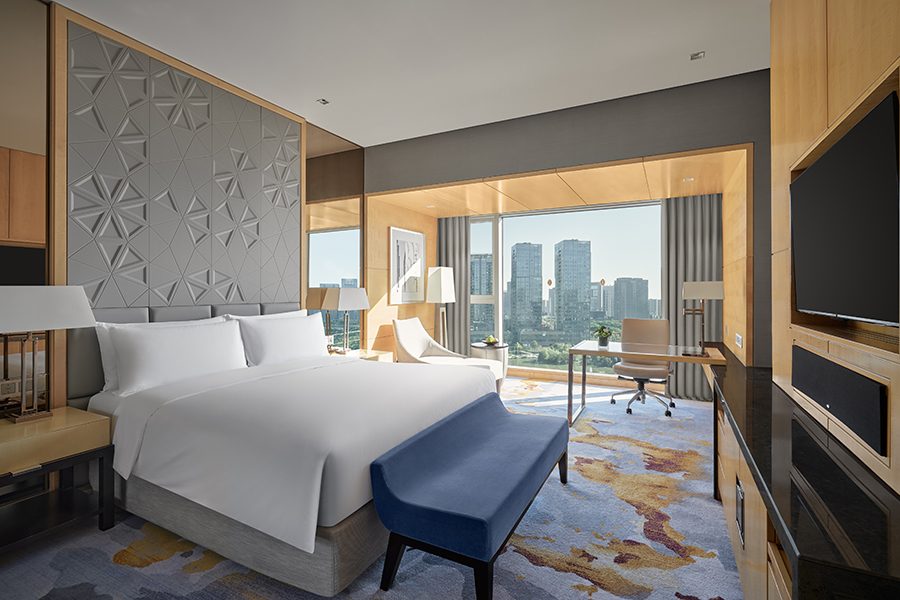 An interior view of the elegant designed guestroom with carpeted floors, artistic wall panels and city views during daytime 