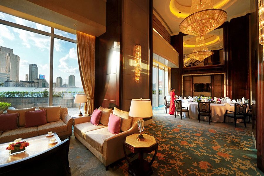 An interior view of an elegant lounge and dining room with sofas next to a large window featuring a city view during daytime at Shangri-La Ningbo, China 