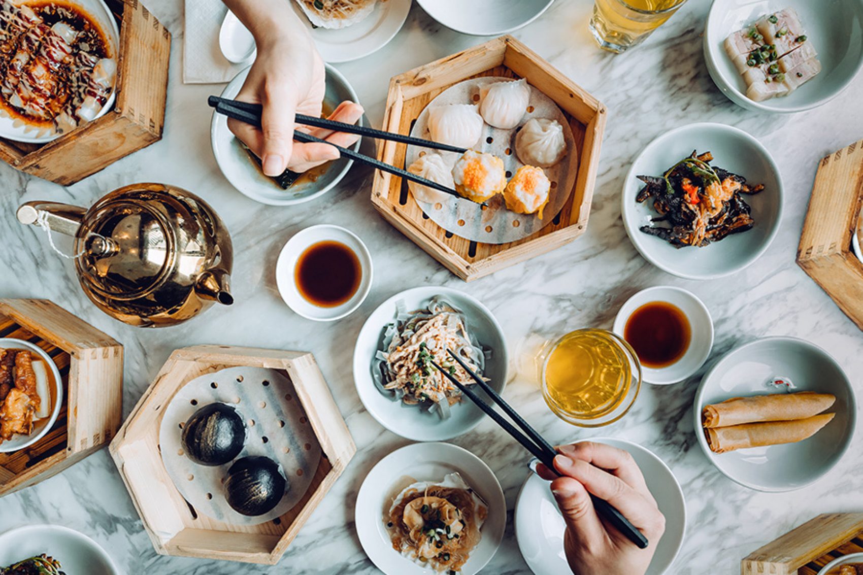 A diner picking up siu mai with chopsticks from a table laden with food, at a dim sum restaurant in Hong Kong.