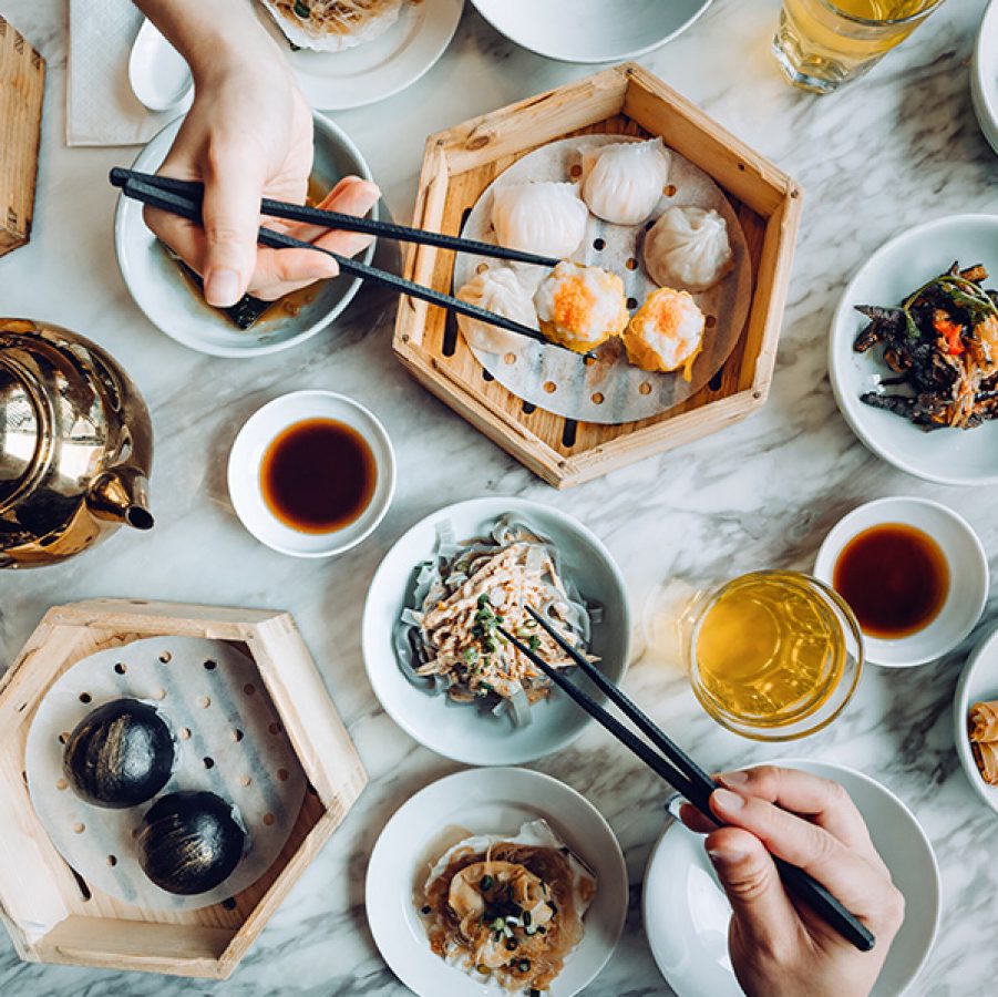 A diner picking up siu mai with chopsticks from a table laden with food, at a dim sum restaurant in Hong Kong.
