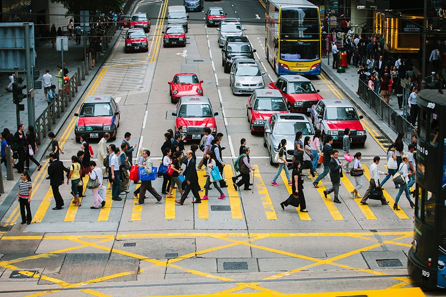 Pedestrians walking at a crossing while red taxis and other vehicles wait at a red light