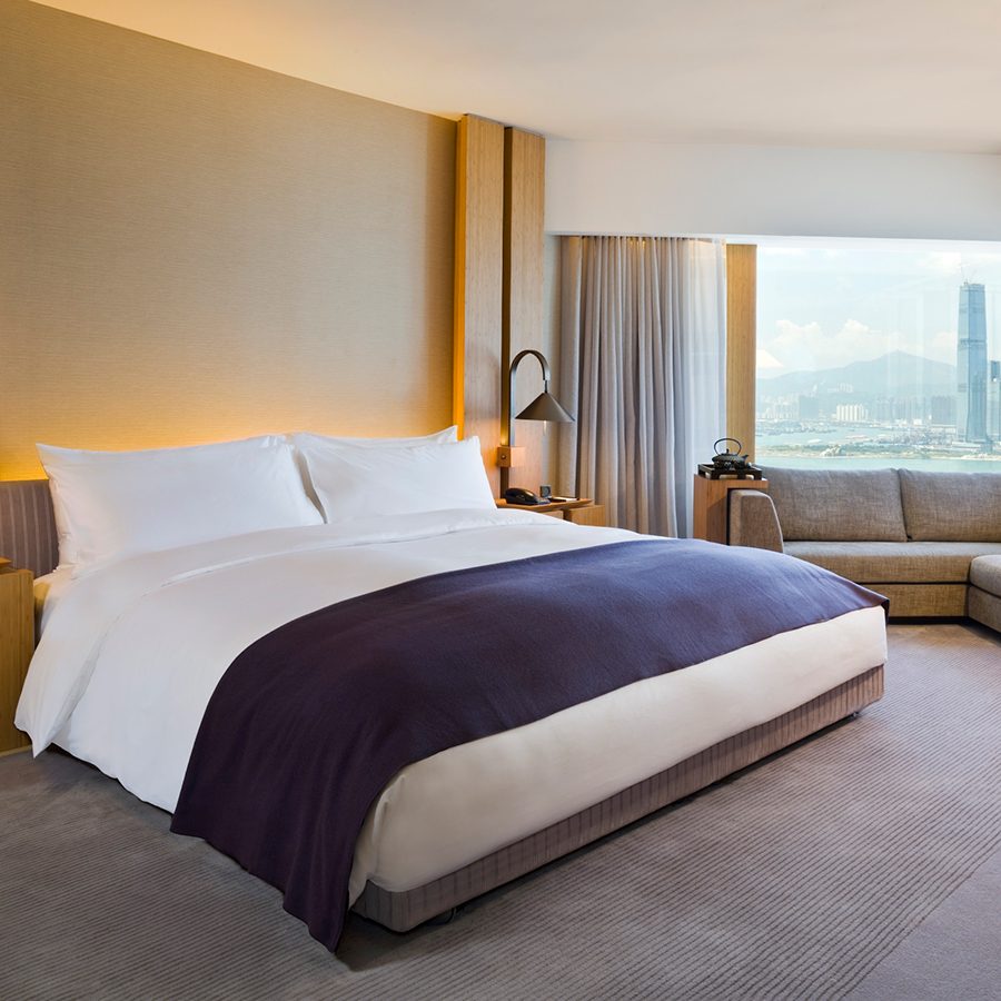 A large bed and sofa in The Upper House’s Studio 70 room with a view of Victoria Harbour. 