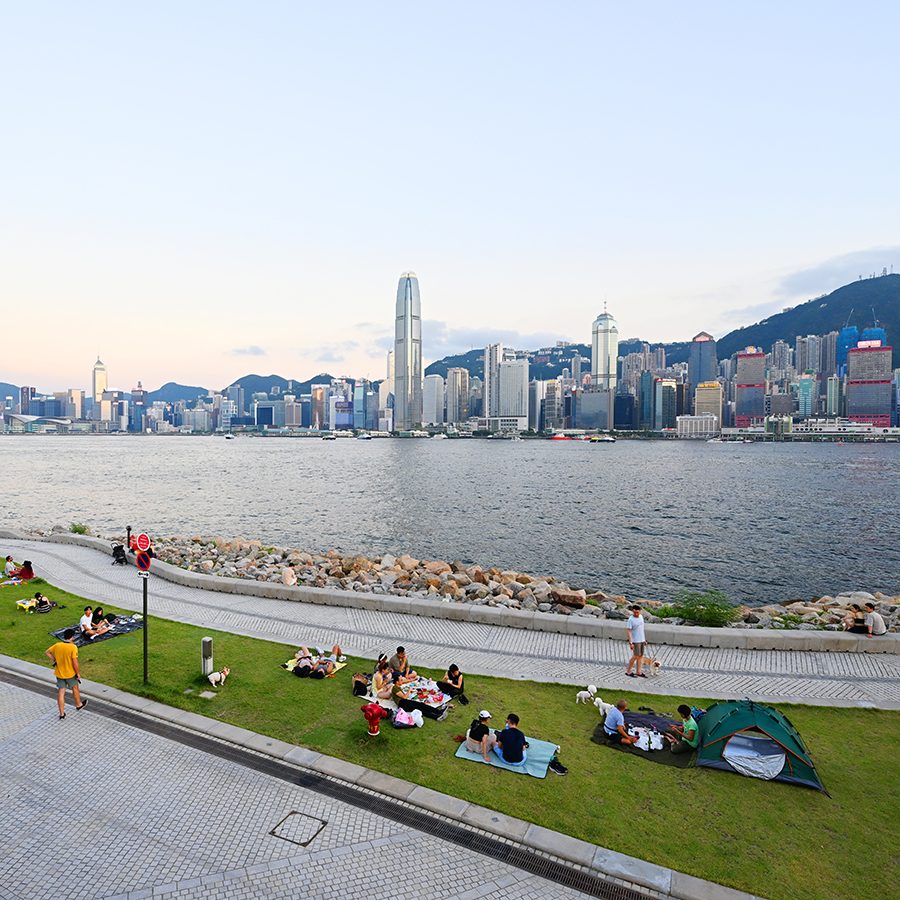 People sitting on the grass at Hong Kong’s West Kowloon Cultural District during nice weather. 