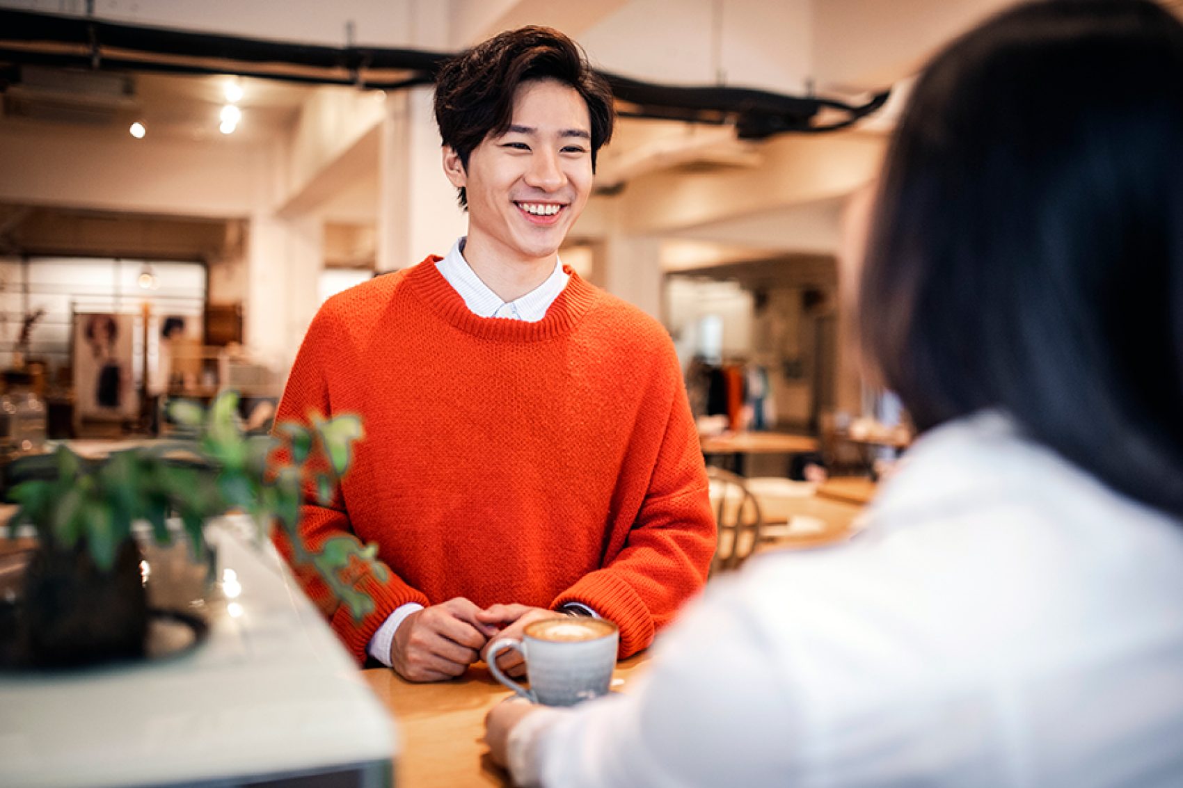 A man smiles at someone in a café during a conversation. 