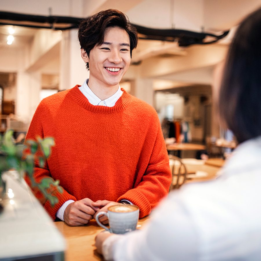 A man smiles at someone in a café during a conversation. 