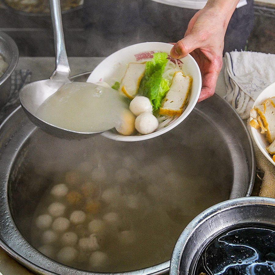A server pours broth onto a bowl of fishball noodles in Hong Kong.