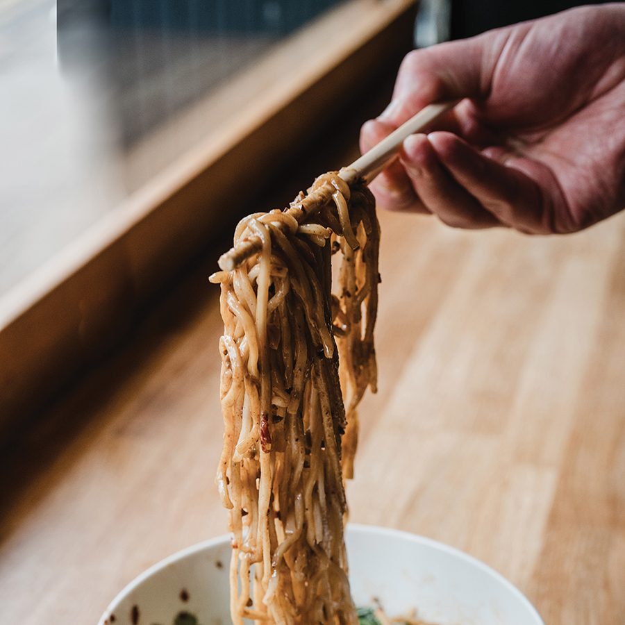 A hand holding chopsticks over a bowl of dan dan noodles at Yikouchi, Birmingham