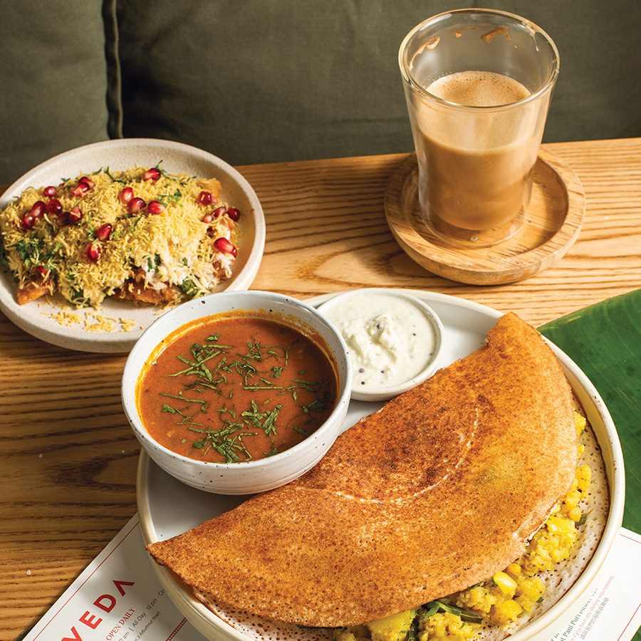 Three Indian dishes on a table at Veda, which includes a dosa, another dish and a drink 
