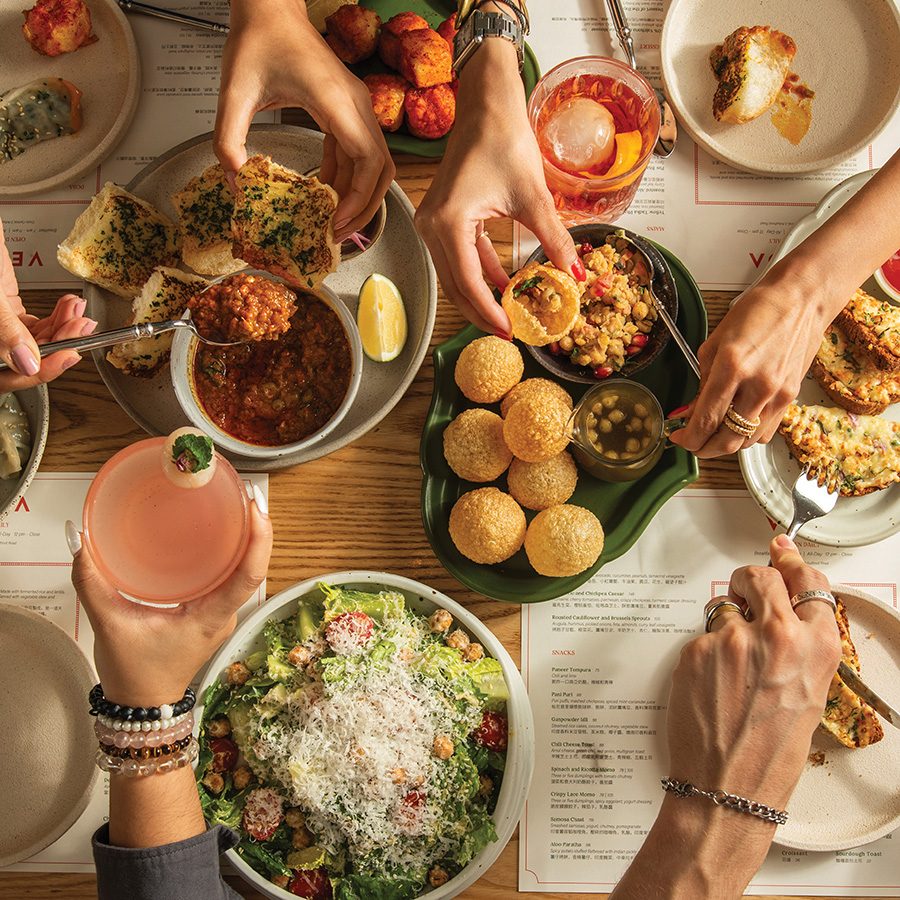 A top-down image of people using hands to exchange food over a table of dishes at Veda Café & Bar 