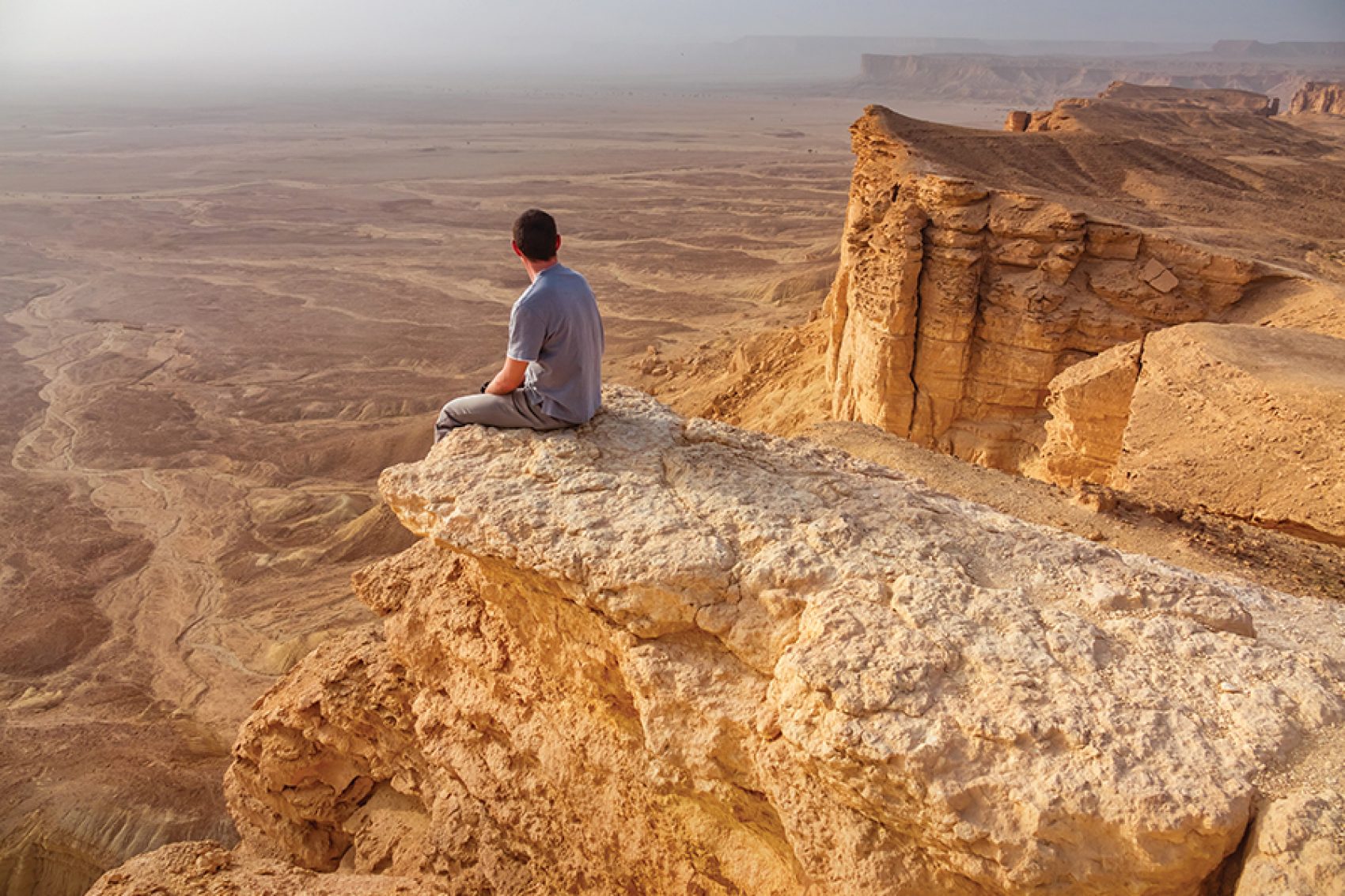 A person sitting on the Edge of the World, a monumental ridge overlooking panoramic desert views 