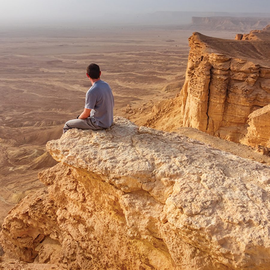 A person sitting on the Edge of the World, a monumental ridge overlooking panoramic desert views 