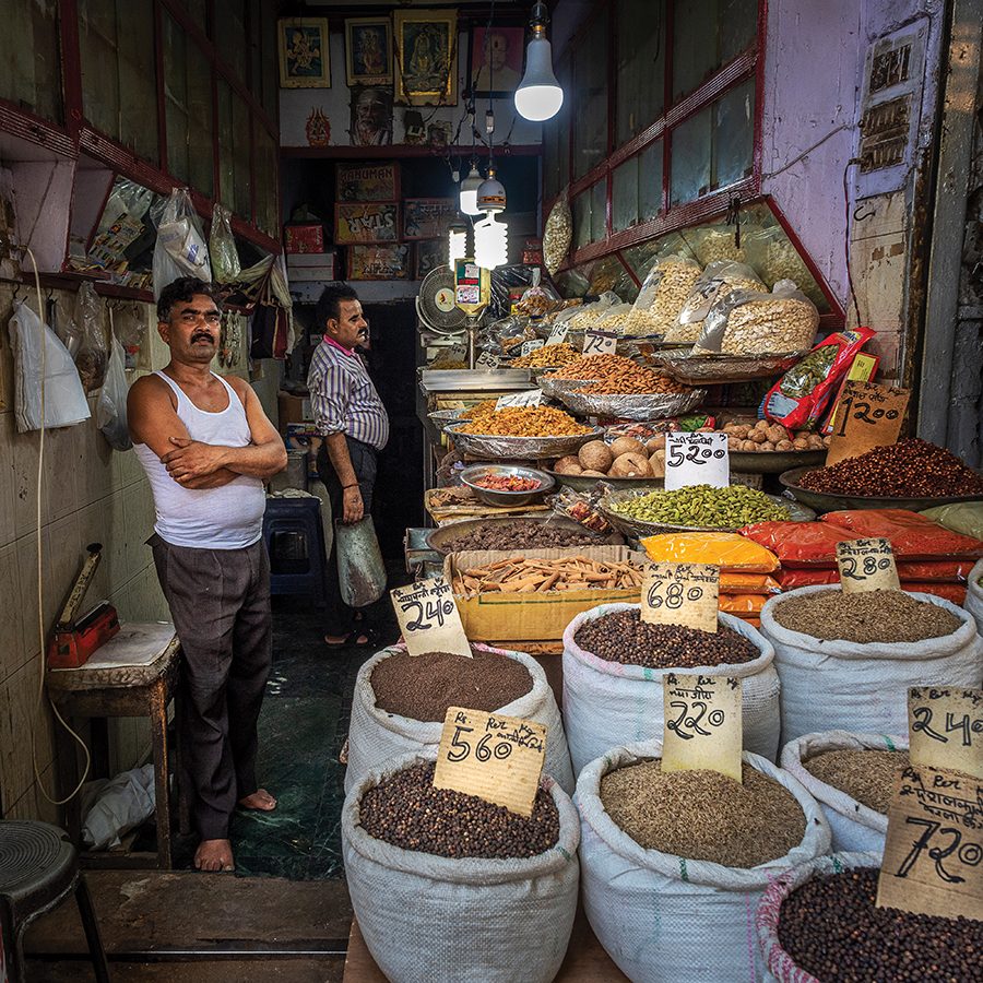 Two men standing in Chandni Chowk market surrounded by bags of spices