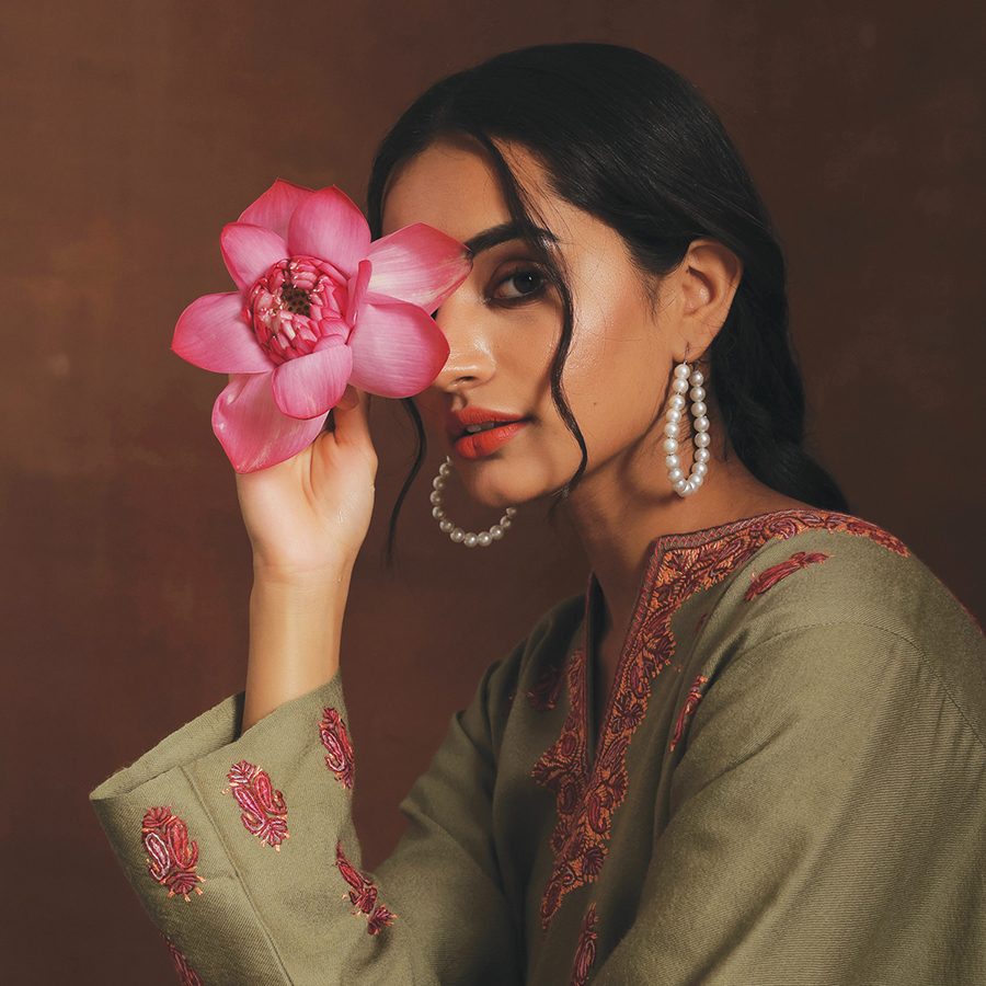 A woman dressed in a hand-embroidered wool phiran from KCS Kashmir Shawl Emporium, holding a lotus
