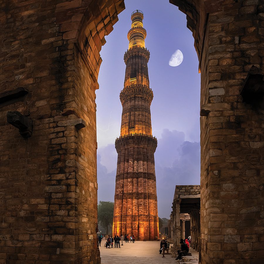 Qutub Minar with the moon next to it, seen through an arch