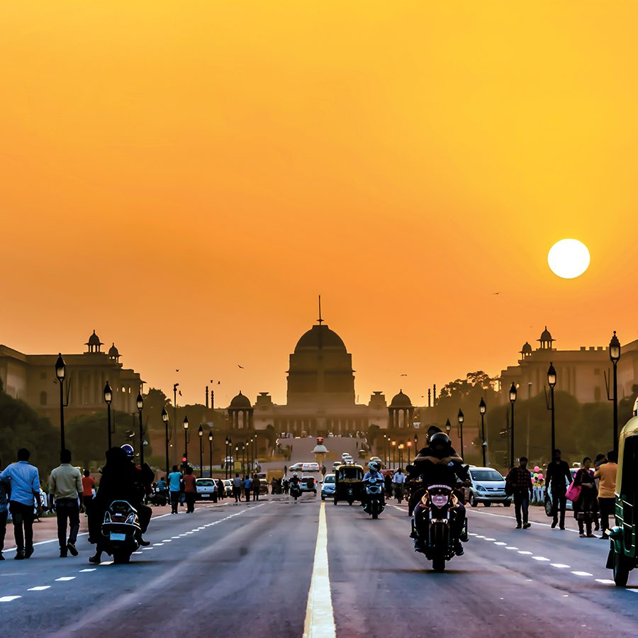 A busy road in Delhi with people and cars and Rashtrapati Bhavan in the background