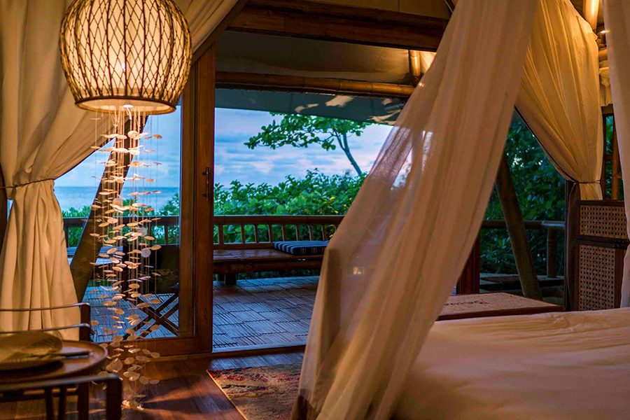 A bedroom with a balcony overlooking trees and the ocean at Bawah Reserve, Indonesia