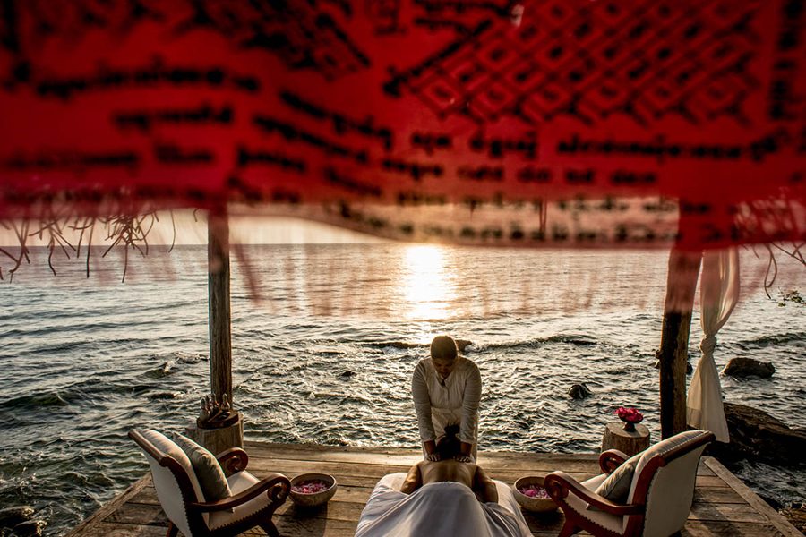 A person lying on a massage table receiving a shoulder rub from a massage therapist with a view of the ocean in the background at Song Saa Private Island, Cambodia