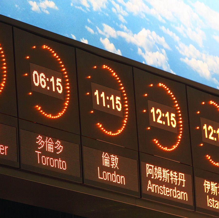 A digital display against a blue sky showing the time and city names in English and Chinese. The cities are Vancouver, Toronto, London, Amsterdam, Istanbul and Doha. 