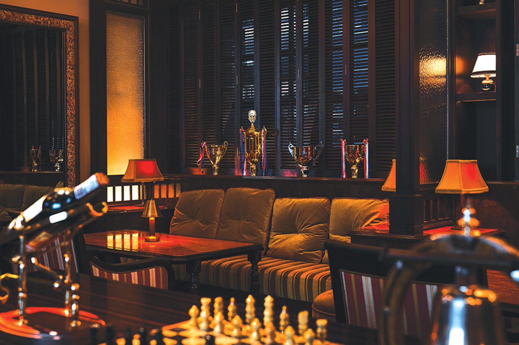  The interior of Jack’s Racquet Room, which includes a couch and coffee table, a chess board, sports trophies and a bottle of wine