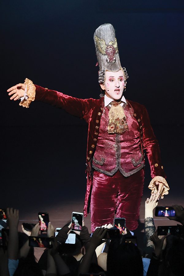An actor in Mozart, L’Opéra Rock dressed in red velvet attire and a Baroque wig