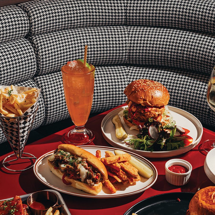 A red table at American diner RightSideUp filled with food and drinks like burgers, hot dogs, and fries in front of a houndstooth booth